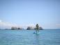 Žena stojaca na paddleboarde v mori s kameňmi v pozadí.