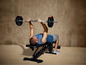 Muž robí bench press s činkou a závažím.