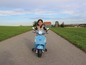 Dievča jazdí na modrej Vespa skútri po štrkovej ceste.