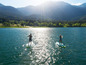 Dvaja ľudia paddleboarding na jazere s pohľadom na hory.