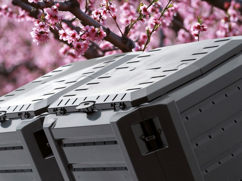 Dve čierne kompostéry pred rozkvitnutými ružovými kvetmi.