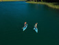 Dve osoby pádlujú na nafukovacích paddleboardoch na jazere.
