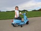 Dievča sedí na modrej Vespa-podobnej motorke.
