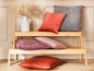 Drevená lavica s rôznymi vankúšmi v červenej, ružovej a sivej farbe.