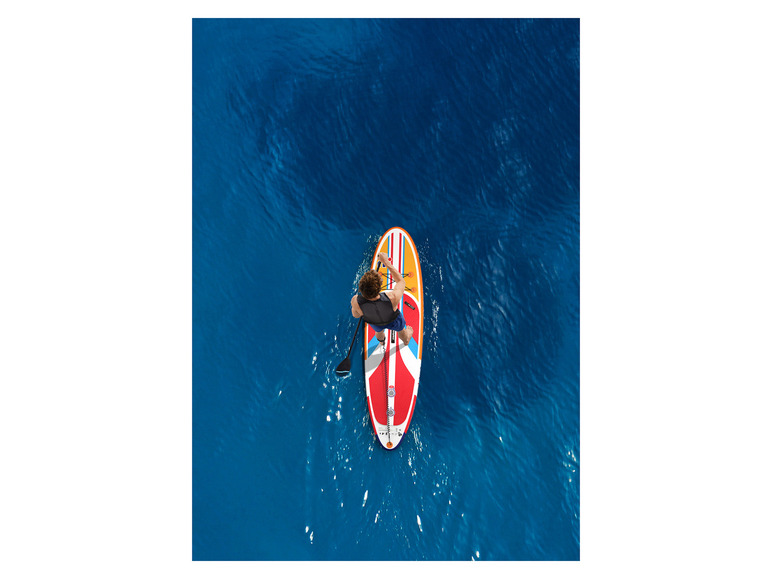 Osoba pádlujúca na nafukovacom paddleboarde s oranžovou a červenou farbou v mori.