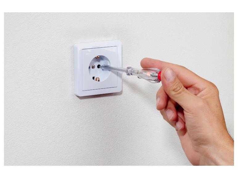 Ruka drží skúšačku napätia v elektrickej zásuvke.