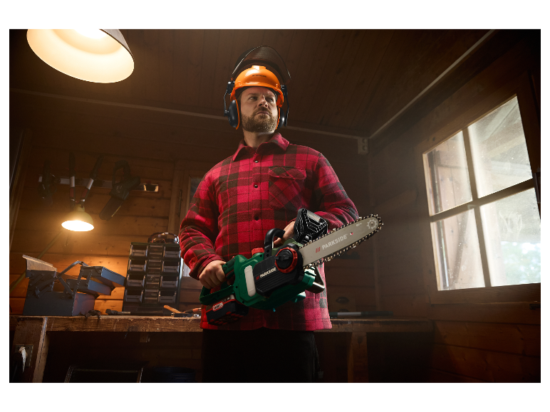 Muž v prilbe a chráničoch sluchu drží motorovú pílu Parkside.