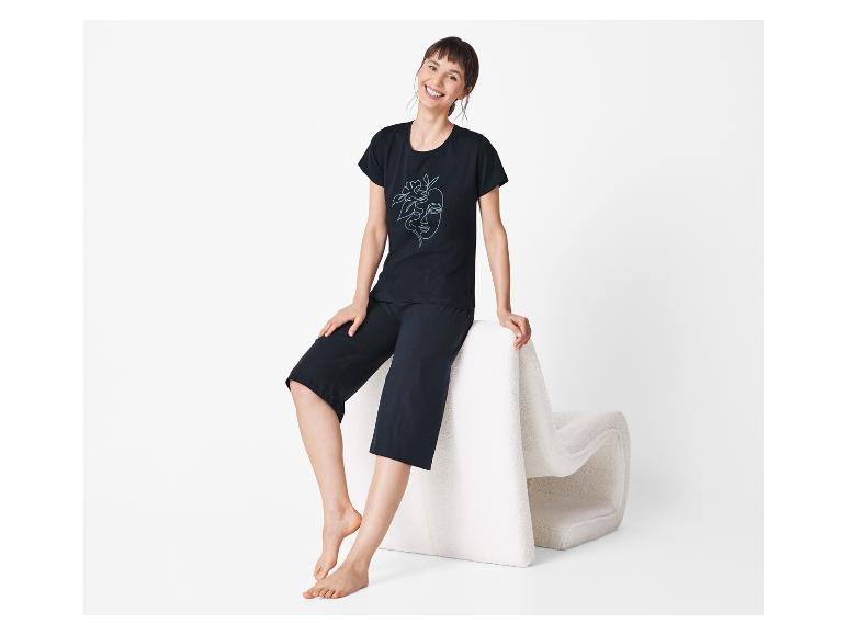 Žena v čiernom pyžame s potlačou sedí na bielom pufe.