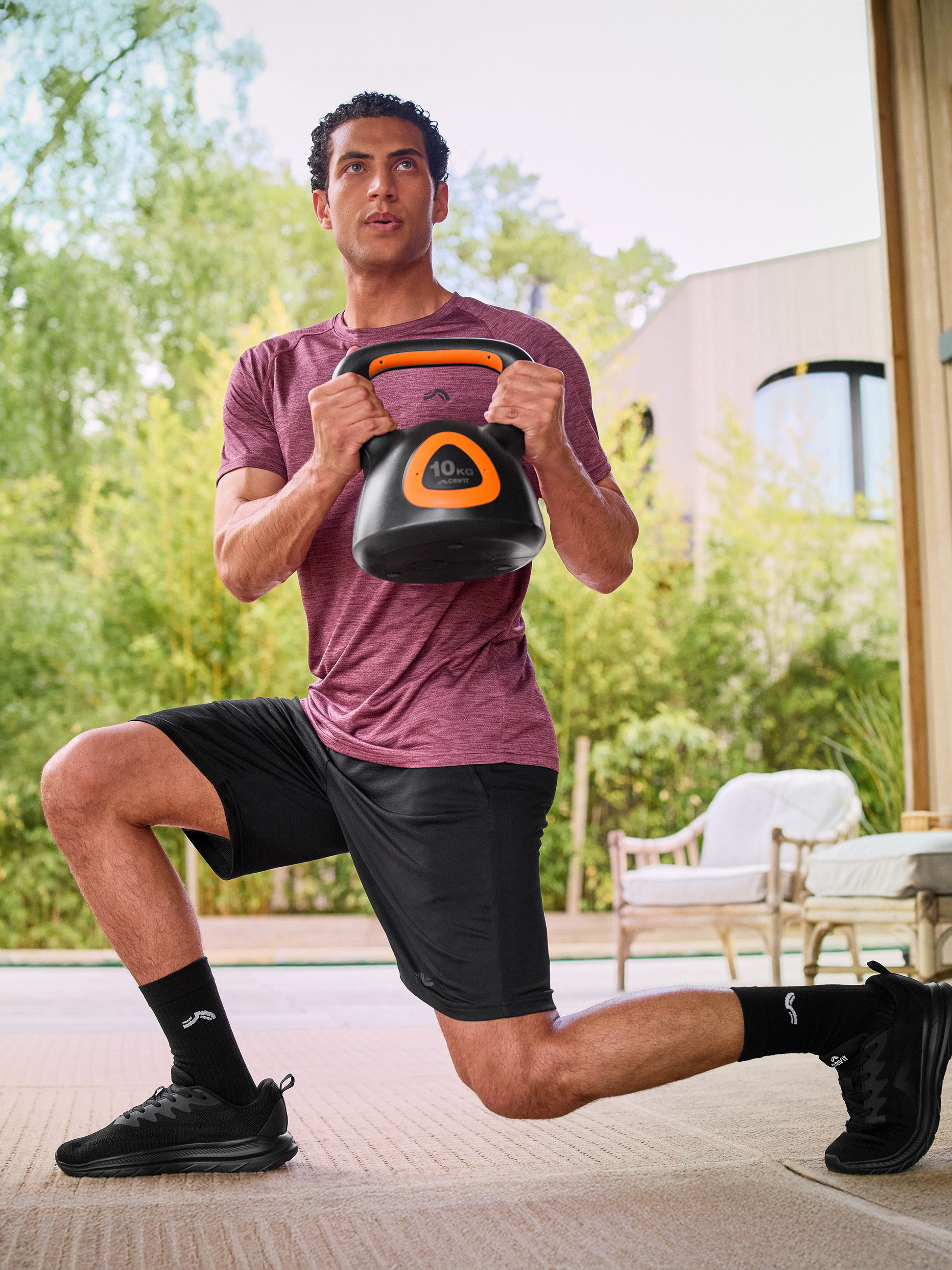Muž v športovom oblečení robí výpad s čiernym 10 kg kettlebellom.