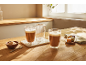 Dve poháre latte a sladkosti na drevenom stole.
