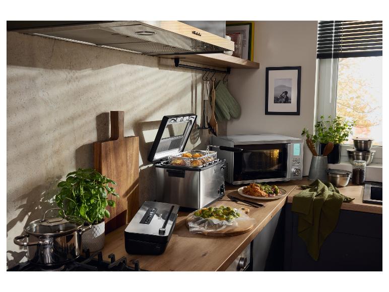 Kuchyňa s fritézou, mikrovlnnou rúrou, vákuovou zváračkou a hrncami na drevenej doske.