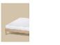 Biely matrac na svetlom drevenom ráme postele na béžovom pozadí.