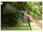 Ruka drží zelenú striekaciu pištoľ, ktorá strieka vodu v záhrade.
