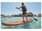 Muž na červenom SUP paddleboarde pádluje v mori, v pozadí skaly.
