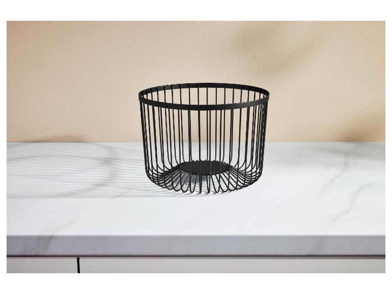 Čierny drôtený kôš na ovocie na bielej mramorovej doske s béžovou stenou