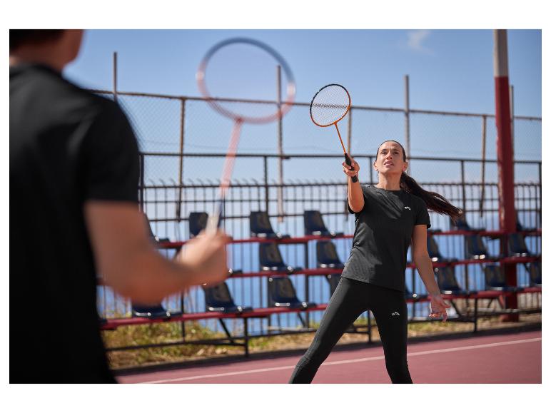 Žena a muž hrajú bedminton na vonkajšom kurte, oblečení v čiernom športovom oblečení.