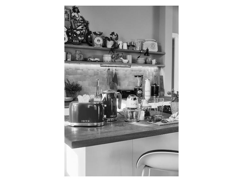 Chlebár, kanvica a ďalšie kuchynské spotrebiče v štýle 1973 na drevenom stole.