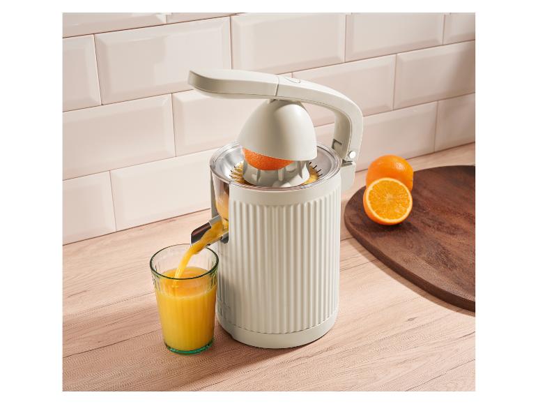 Elektrický odšťavovač citrusov nalieva čerstvú pomarančovú šťavu do pohára na kuchynskej linke.