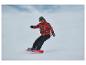 Snowboardista v červenej vzorovanej bunde a čiernych nohaviciach, na červenom snowboarde.