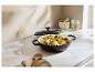 Čierny liatinový hrniec s pokrievkou, plný pečených zemiakov a húb, na kuchynskej linke.