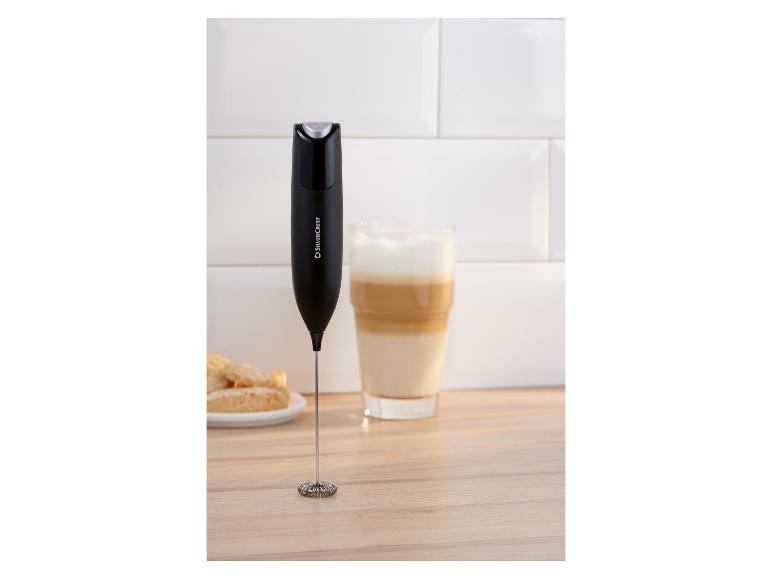 Čierny napeňovač mlieka na drevenom povrchu vedľa pohára latte a sušienok