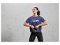 Žena v modrom športovom tričku s nápisom 'Break the Limits' drží čiernu kettlebell.