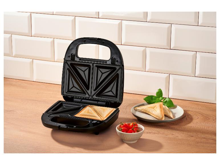 Otvorený sendvičovač s hotovými toastami, paradajkami a bazalkou.