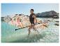 Žena v záchrannej veste s paddleboardom a pádlom vo vode.