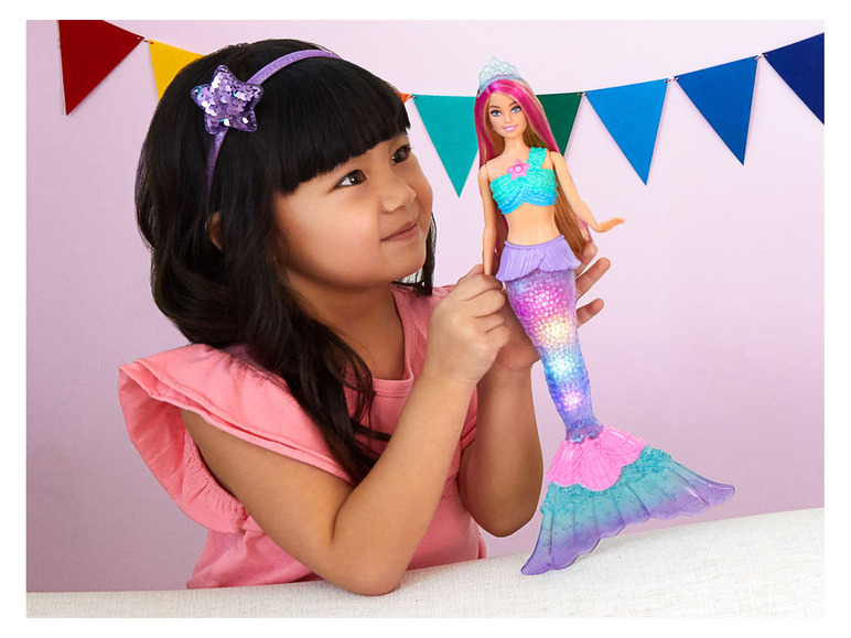 Dievča drží v ruke svietiacu bábiku Barbie morskej panny.