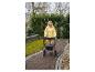 Staršia žena v žltej bunde kráča s chodítkom po dláždenej ceste.