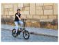 Žena s prilbou jazdí na čiernom skladacom elektrobicykli po dláždenej ulici.