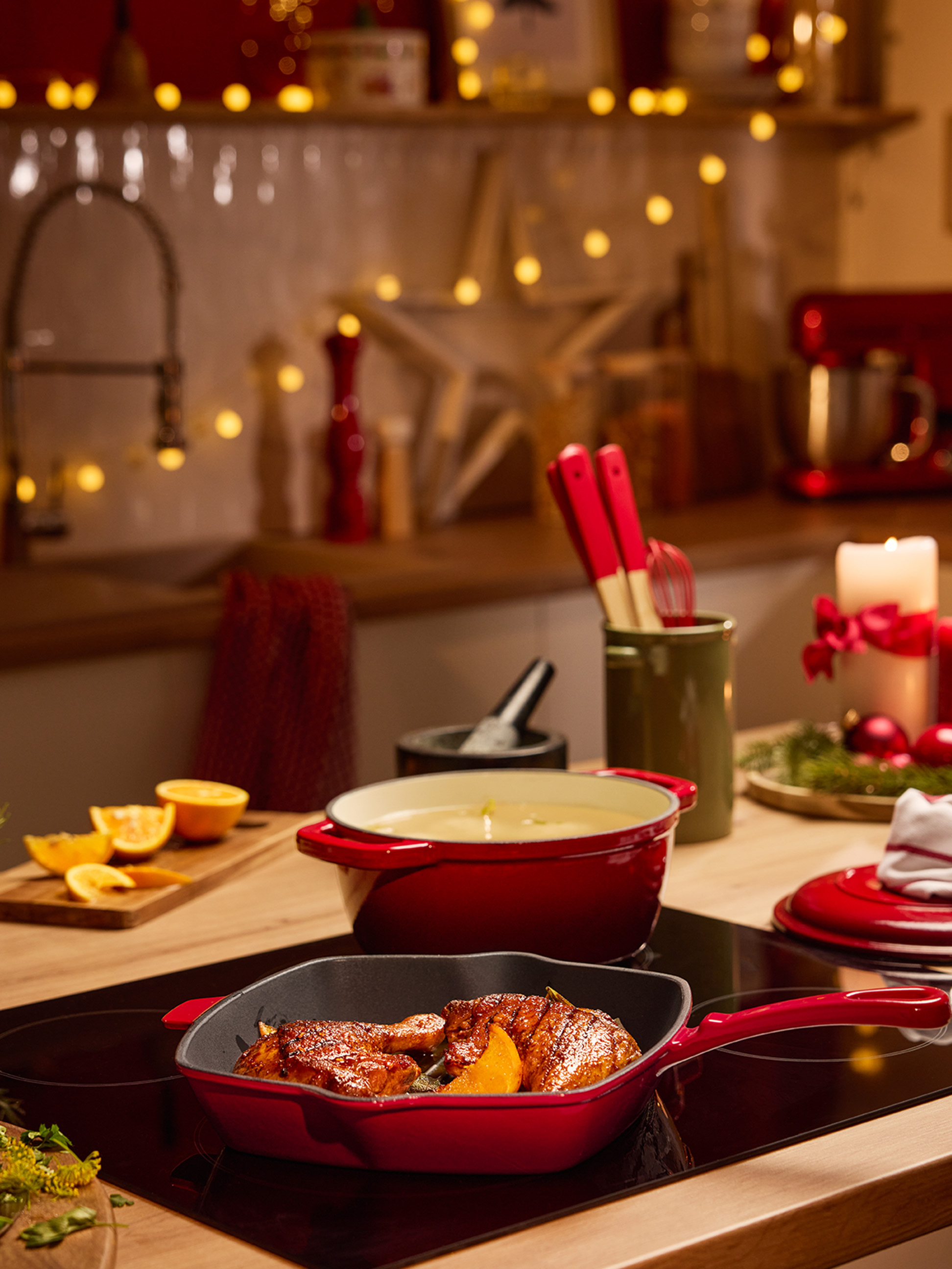 Červené hrnce a panvice s jedlom na varnej doske vo vianočne vyzdobenej kuchyni.