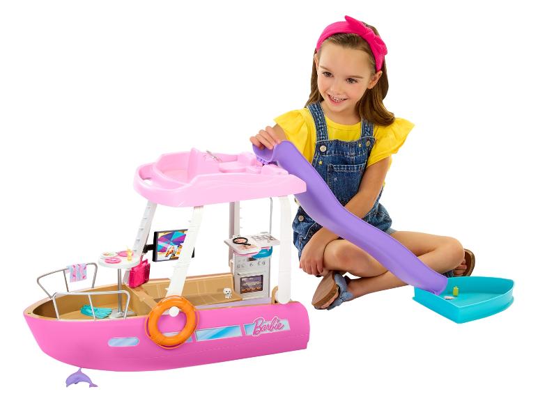 Usmievajúce sa dievča sa hrá s ružovou hračkárskou loďou Barbie, so šmýkačkou a doplnkami.