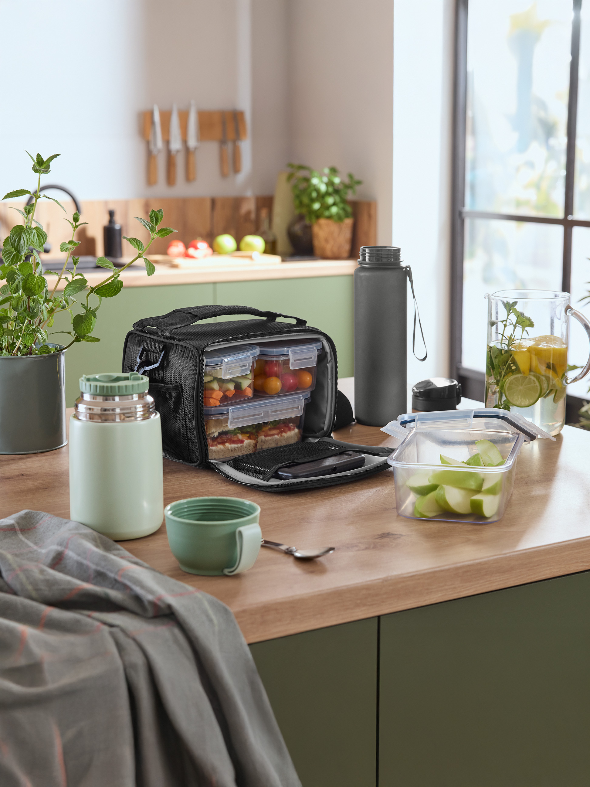 Obedová taška s nádobami na jedlo, termoskou a fľašou na vodu na kuchynskej linke.