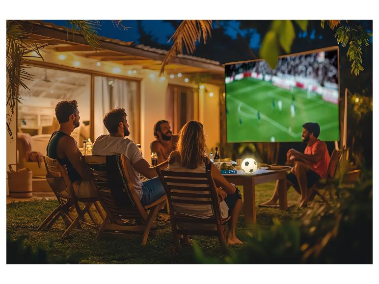 Priatelia sledujú futbalový zápas vonku na veľkej obrazovke v noci.