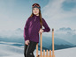 Dievča v purpurovom svetri a čiernych nohaviciach sa opiera o drevené sane pred horským prostredím.