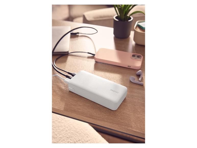 Biela powerbanka nabíja notebook a smartfón na drevenom stole.