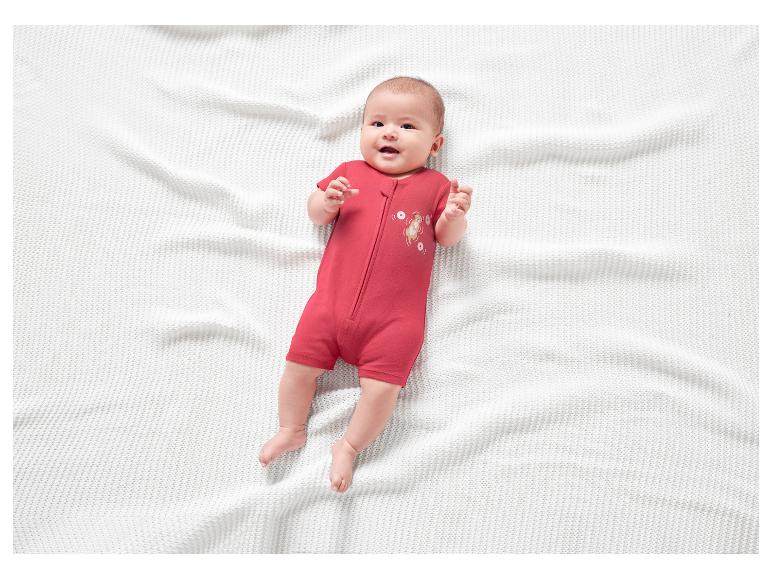 Usmievavé bábätko v červenom dupačkách na bielej deke.