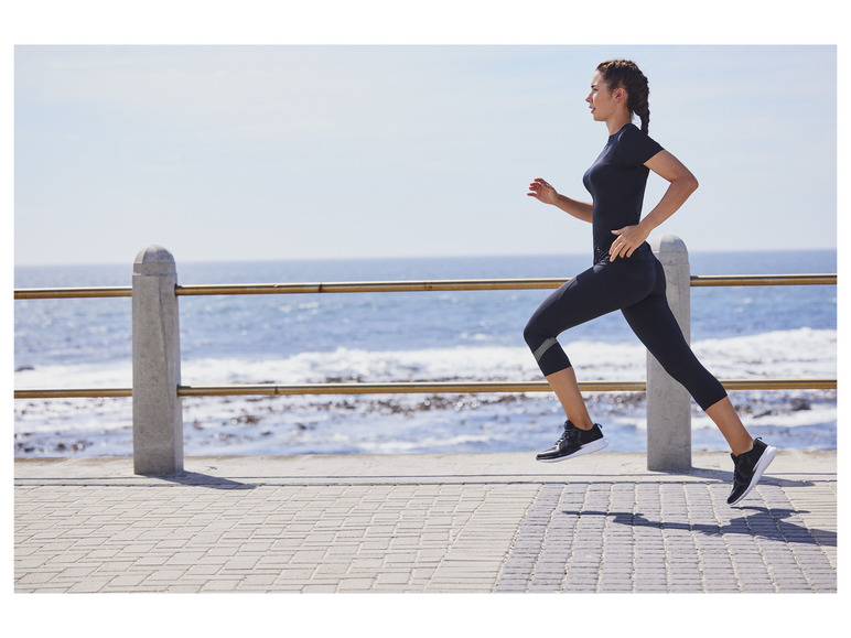 Žena v športovom oblečení beží pozdĺž pobrežia.
