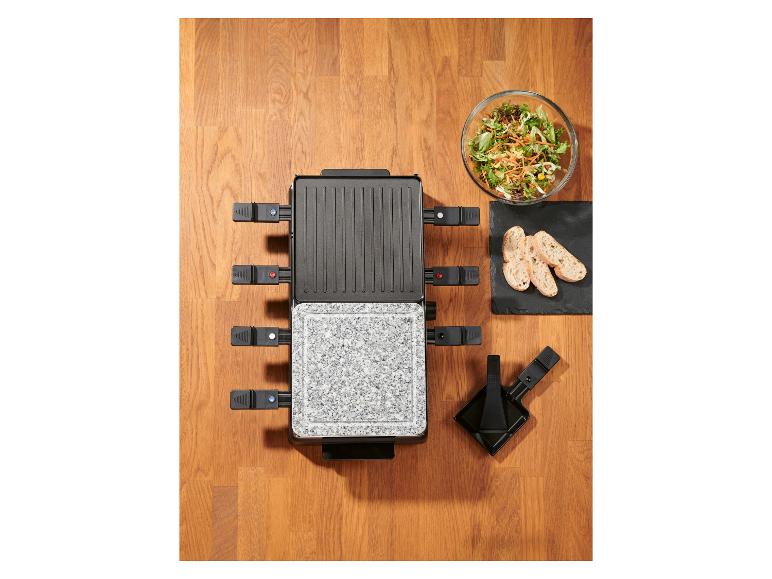 Raclette gril so šalátom a chlebom na drevenom stole.