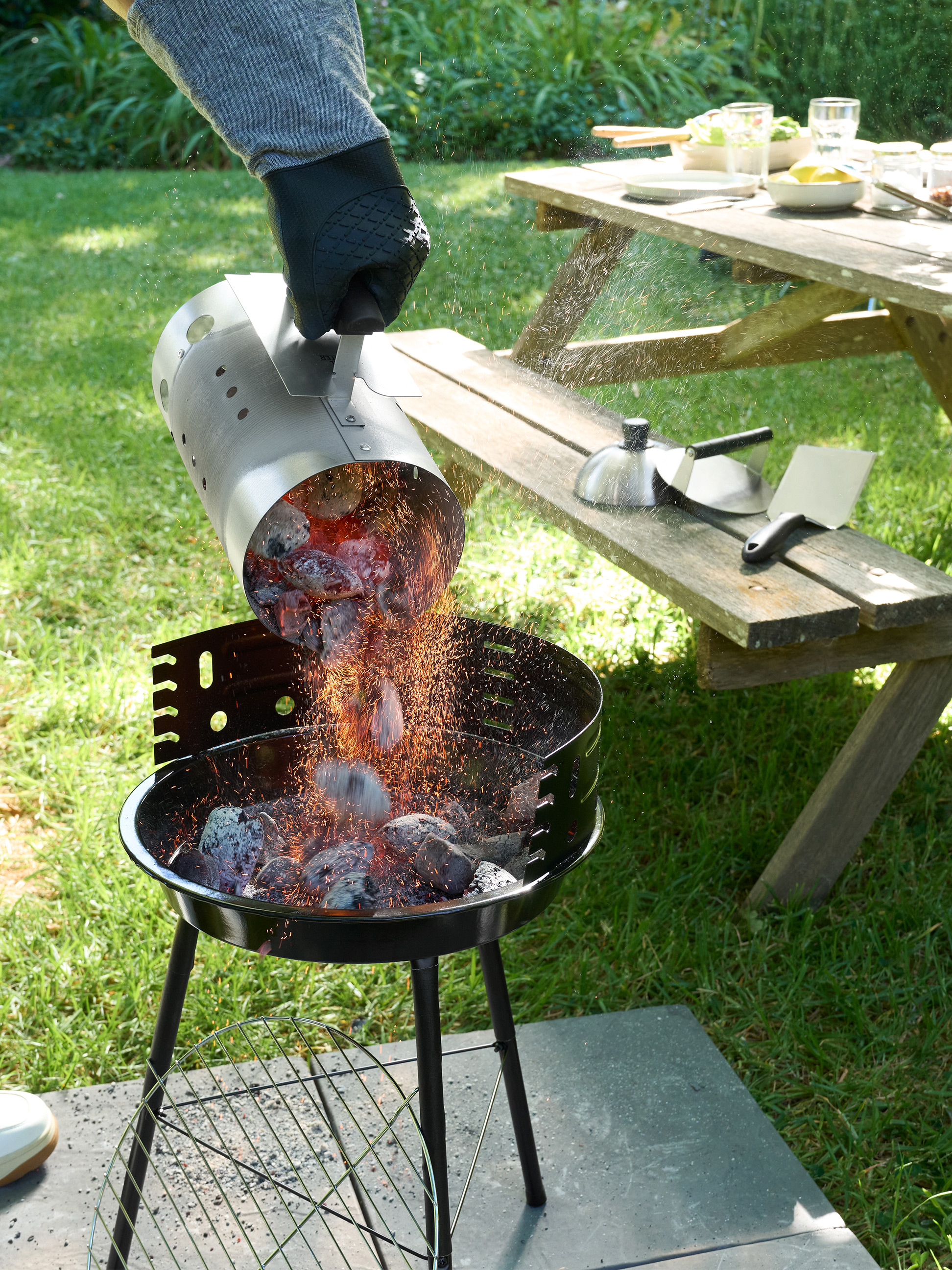 Žeravé uhlie sa sype z podpaľovacieho komína do grilu na drevené uhlie v záhrade.