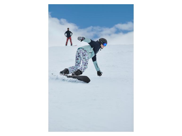 Snowboardista v vzorovaných nohaviciach a svetlomodrej bunde klesá po zasneženom svahu.