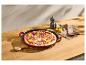 Pizza so salámou, červenou cibuľou a paprikou v liatinovej panvici na drevenom stole.