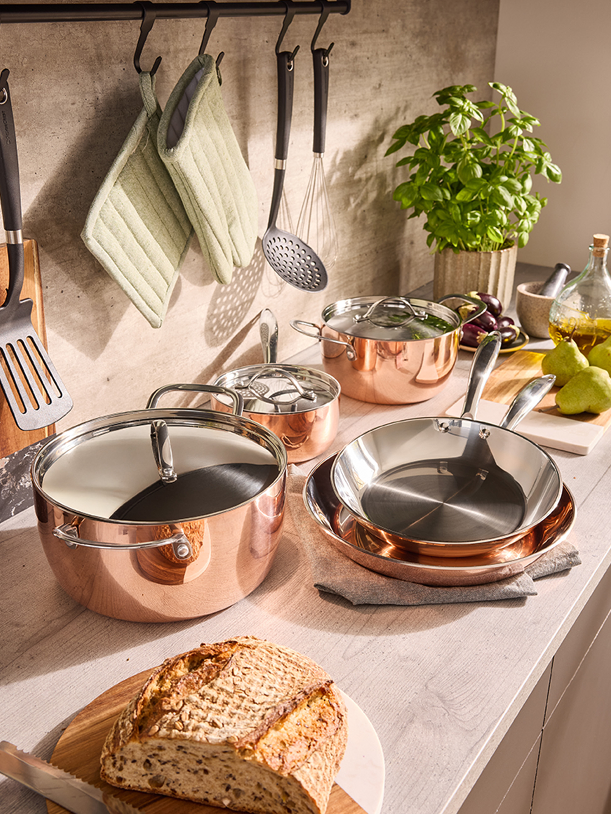 Sada medeného riadu a panvíc na kuchynskej linke, s chlebom a bylinkami.