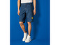 Muž v modrých denimových šortkách s logom Lidl a bielych teniskách.
