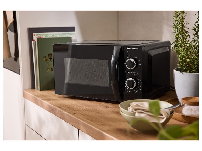 Čierna mikrovlnná rúra Silvercrest na drevenej doske s kuchárskymi knihami a rastlinou.