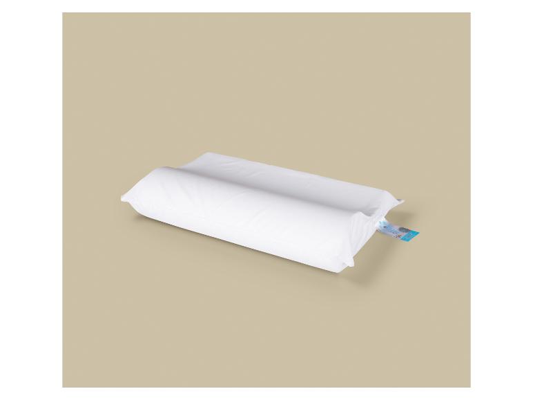 Biela ortopedická poduška s modrou etiketou na béžovom pozadí.