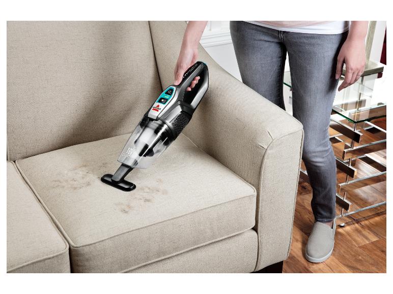 Žena čistí látkovú pohovku ručným vysávačom Bissell