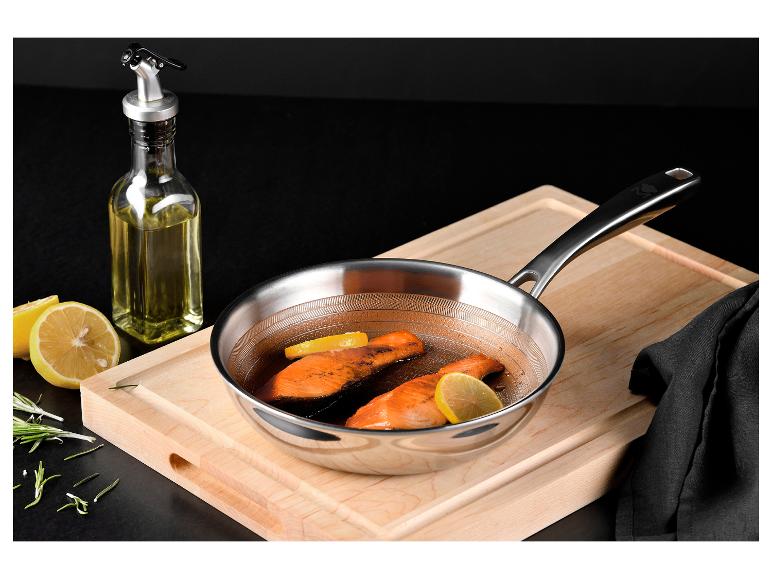 Nerezová panvica s lososom, citrónom a rozmarínom na drevenej doske na krájanie.