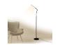 Moderná čierna stojaca lampa osvetľujúca sivé kreslo v minimalistickom interiéri.
